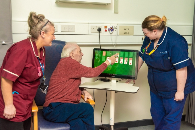 A photo of two clinicians and a patient playing solitaire