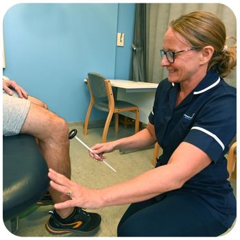 A clinician is kneeling on the floor holding the knee of a patient who is seated. You can only see the patient's knee and not the full body.